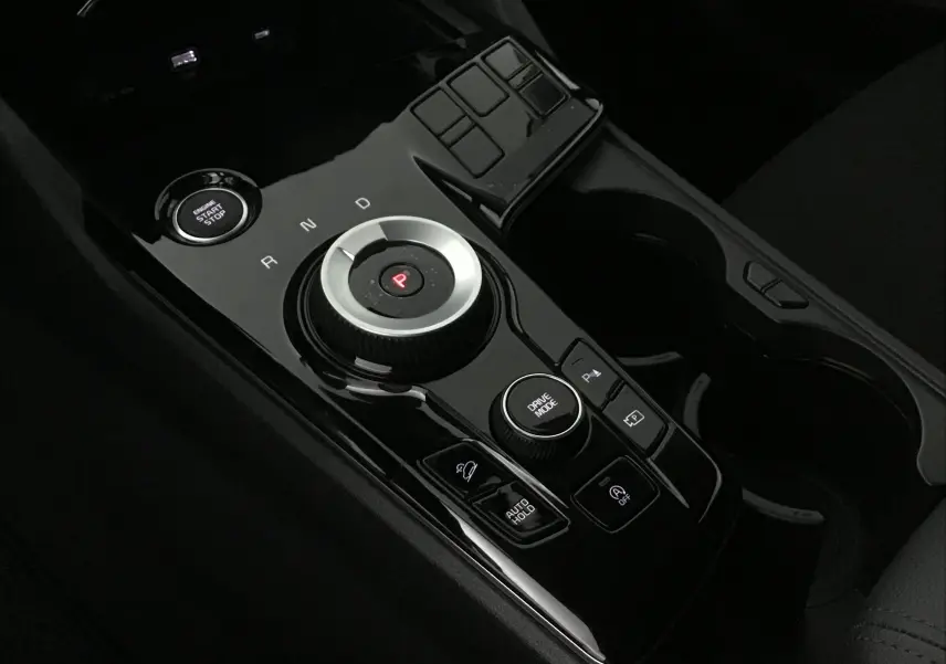 Gros plan sur la console centrale noire brillante du Kia Sportage 2025 avec molette de boîte auto et bouton start/stop.