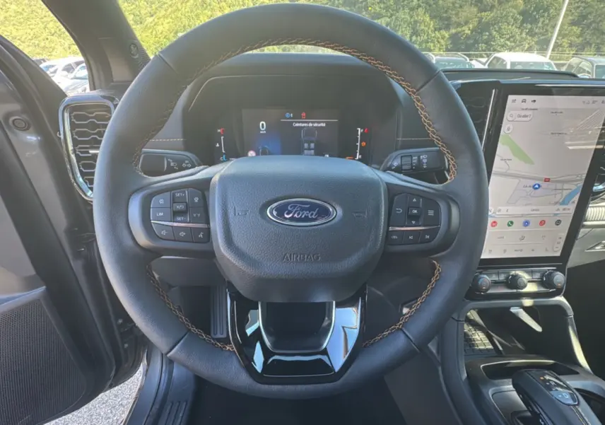 Vue intérieure centrée sur le volant noir avec surpiqûres marron du Ford Ranger 2025 gris carbone, écran tactile et tableau de bord digital visibles.