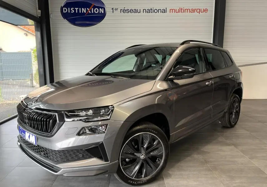 Vue 3/4 avant droite d'un SUV SKODA KAROQ gris métallisé avec jantes alliage noires et calandre noire sportive.