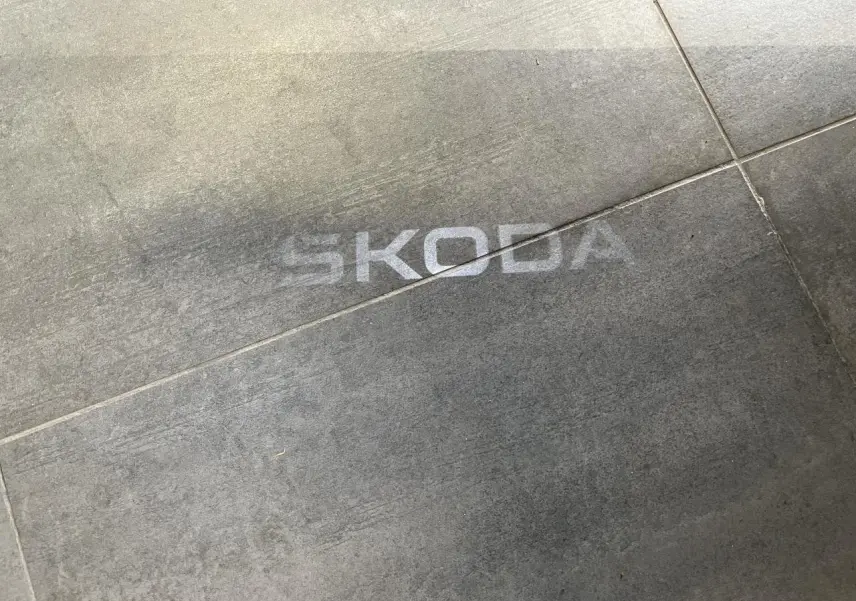 Projection lumineuse du logo SKODA au sol sur surface grise, visible depuis le côté droit du véhicule gris.