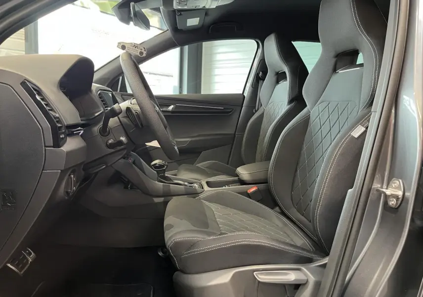 Vue intérieure côté conducteur du Skoda Karoq gris 2025, mettant en valeur les sièges sport noirs et le tableau de bord moderne.
