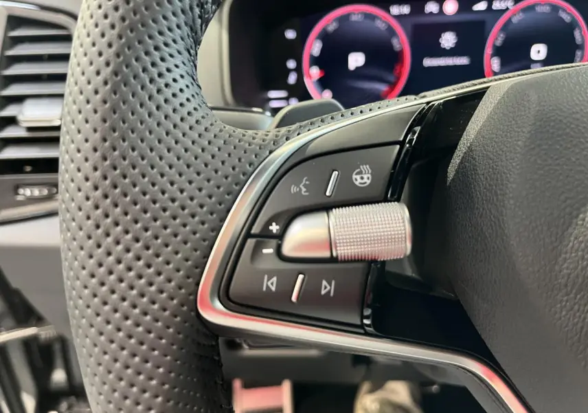 Gros plan sur les commandes gauche du volant perforé noir du Skoda Karoq 2025 avec tableau de bord digital en arrière-plan.