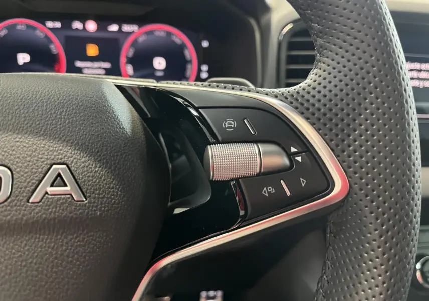 Gros plan sur le volant cuir perforé noir du Skoda Karoq 2025 avec commandes multifonctions et tableau de bord digital rouge.