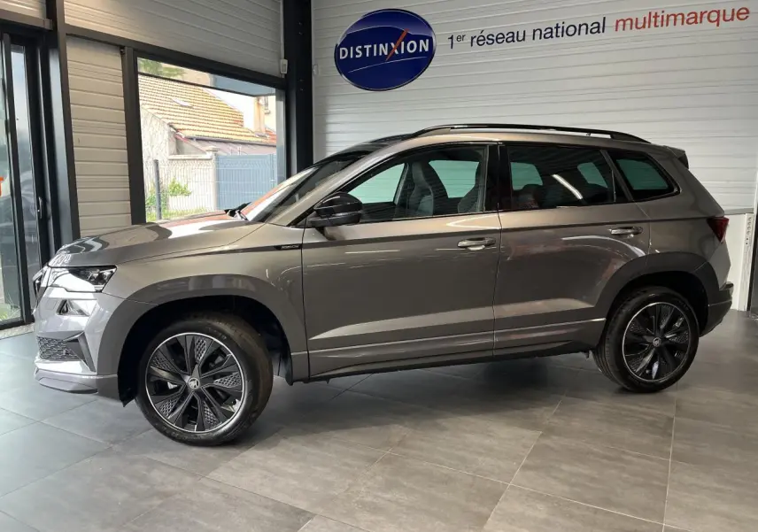 SUV SKODA KAROQ gris en profil droit dans un showroom, avec jantes alliage noires et toit noir.