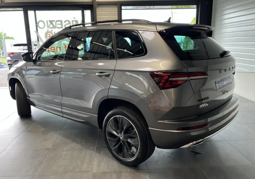 Vue 3/4 arrière droite d'un SUV SKODA KAROQ gris métallisé avec jantes alliage noires et toit noir dans un showroom.