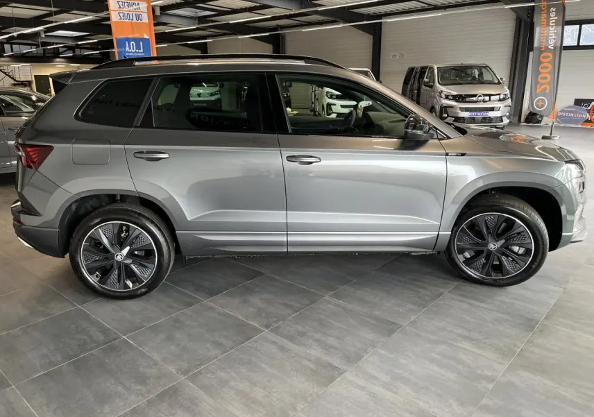 Vue de profil côté gauche du SUV SKODA KAROQ Sportline gris métallisé avec jantes alliage 19'' Sagitarius anthracite en showroom.