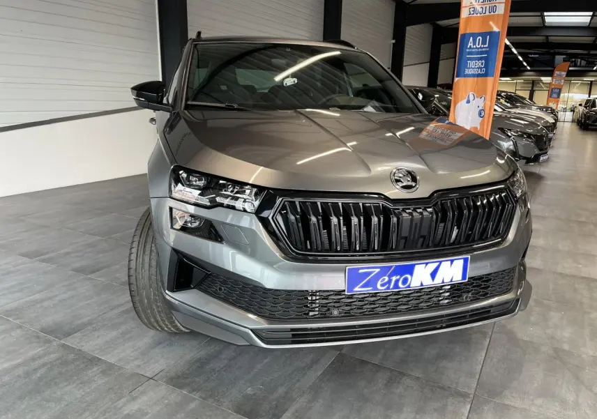 Vue 3/4 avant d'un SUV Skoda Karoq gris métallisé avec calandre noire et phares LED dans un showroom.