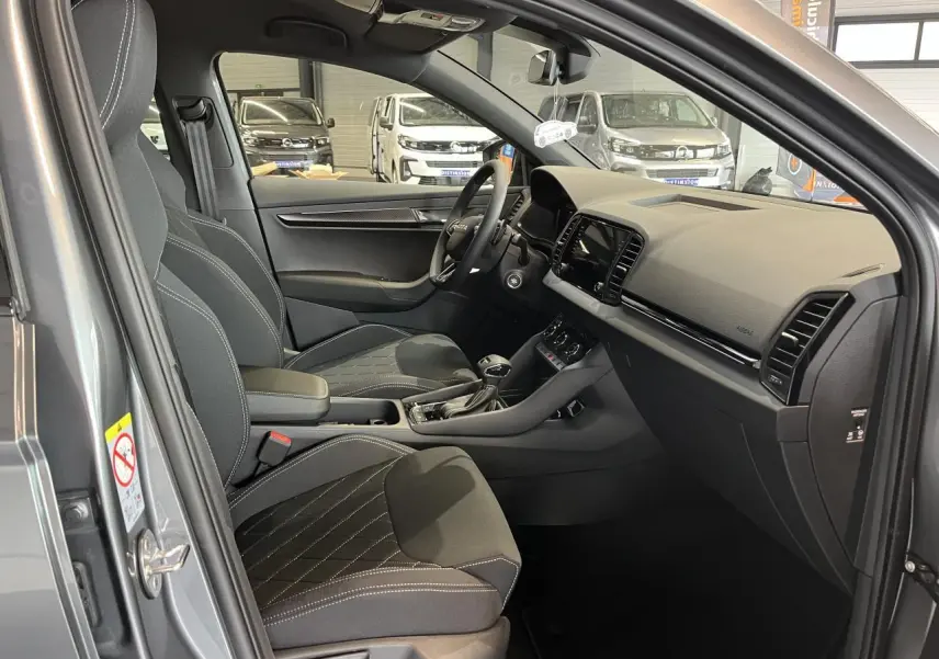 Vue intérieure côté conducteur du Skoda Karoq gris 2025, mettant en valeur les sièges sport noirs et la console centrale moderne.