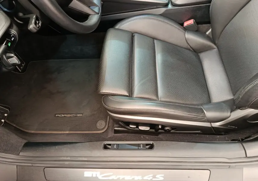 Vue intérieure côté conducteur de la Porsche 911 Carrera 4S 2019, siège cuir noir et tapis avec logo Porsche.
