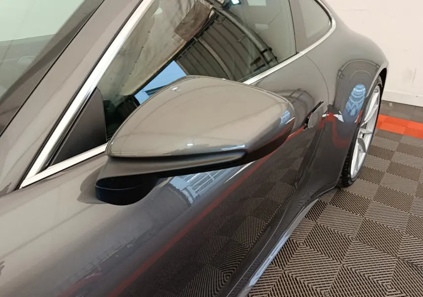 Vue rapprochée du rétroviseur côté gauche d’une Porsche 911 Carrera 4S Coupé gris foncé, avec reflet sur la carrosserie lisse.