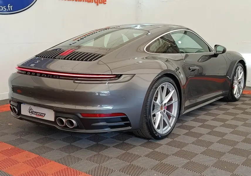 Vue 3/4 arrière droite d'une Porsche 911 Carrera 4S Coupé gris foncé avec quadruple sortie d'échappement et feux LED continus.