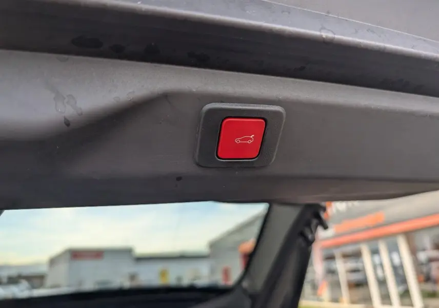 Bouton rouge d'ouverture électrique du hayon visible depuis l'intérieur arrière du Peugeot 3008 blanc 2025.