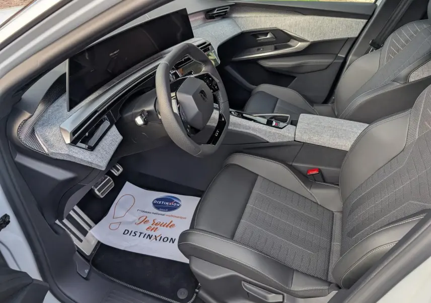 Vue intérieure côté conducteur du Peugeot 3008 GT 2025 blanc, avec sellerie tissu gris et cuir noir, volant compact et tableau de bord numérique.