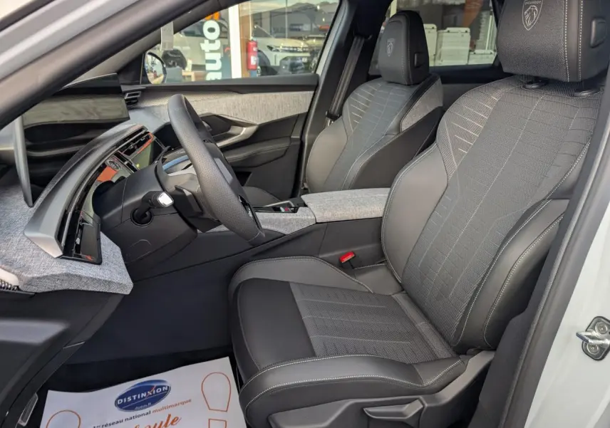 Vue intérieure côté conducteur du Peugeot 3008 blanc 2025, sièges tissu et cuir gris avec logo Peugeot brodé.