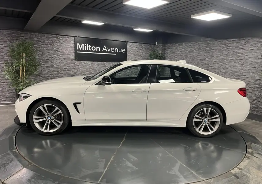 Profil côté gauche d'une BMW Série 4 Gran Coupé blanche avec jantes alliage 18'' en étoile dans un showroom.
