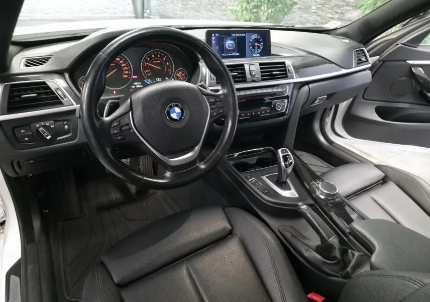 Intérieur BMW Série 4 430i blanc vu côté conducteur, sellerie cuir noire et console centrale avec écran multimédia.