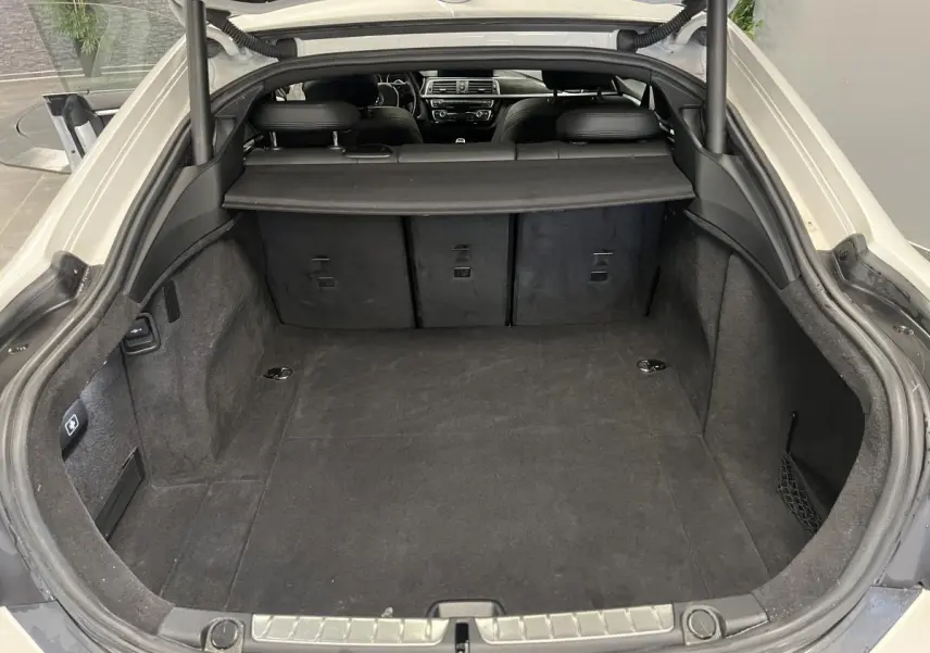 Coffre ouvert d’une BMW Série 4 Gran Coupé blanche, vue intérieure montrant l’espace de chargement et la banquette arrière.