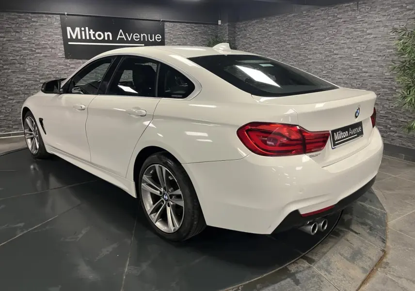 BMW Série 4 Gran Coupé blanc vue 3/4 arrière droit avec jantes alliage 18 pouces et double sortie d’échappement.