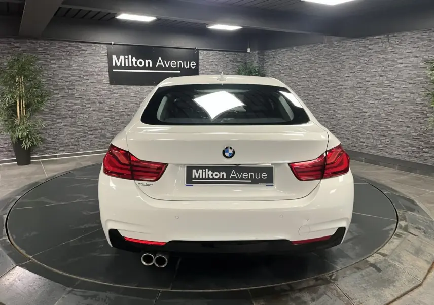 Vue arrière d'une BMW Série 4 Gran Coupé blanche avec double sortie d'échappement et feux arrière LED rouges.