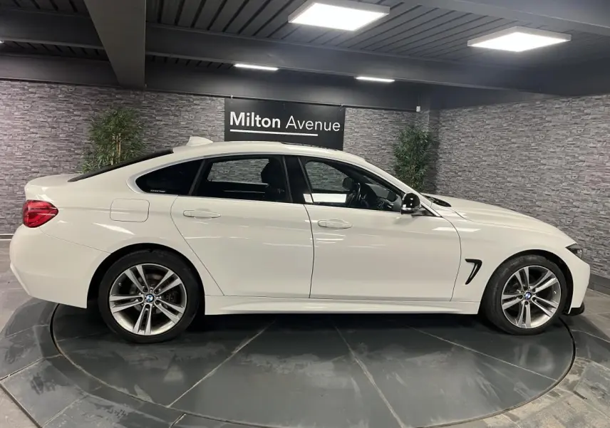 BMW Série 4 430i Gran Coupé blanc vue de profil côté gauche avec jantes alliage 18 pouces en intérieur showroom.