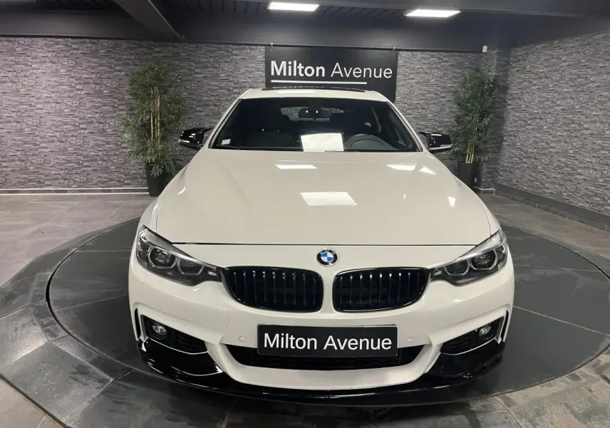 Vue avant d'une BMW Série 4 Gran Coupé blanche avec calandre noire et détails noirs brillants au sol showroom.