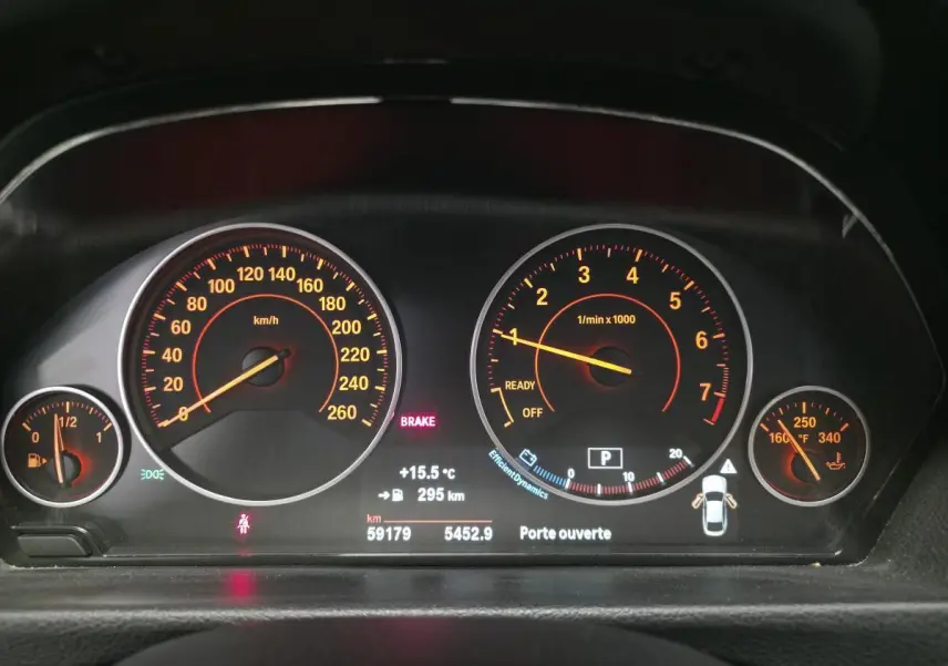 Gros plan sur le tableau de bord numérique de la BMW Série 4 blanc, affichant vitesse, régime moteur et alertes.