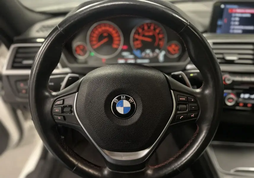 Vue rapprochée du volant cuir noir multifonctions d'une BMW Série 4 430i Gran Coupé, avec tableau de bord éclairé en arrière-plan.