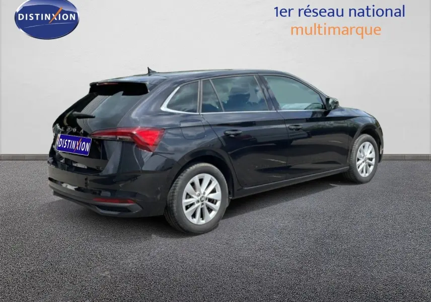 Vue 3/4 arrière droite d'une Skoda Scala noire métal avec jantes argentées, stationnée sur sol gris devant un mur blanc.