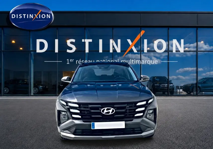 Vue frontale d'un Hyundai Tucson gris ecotronique garé devant une vitrine avec logo Distinxion.