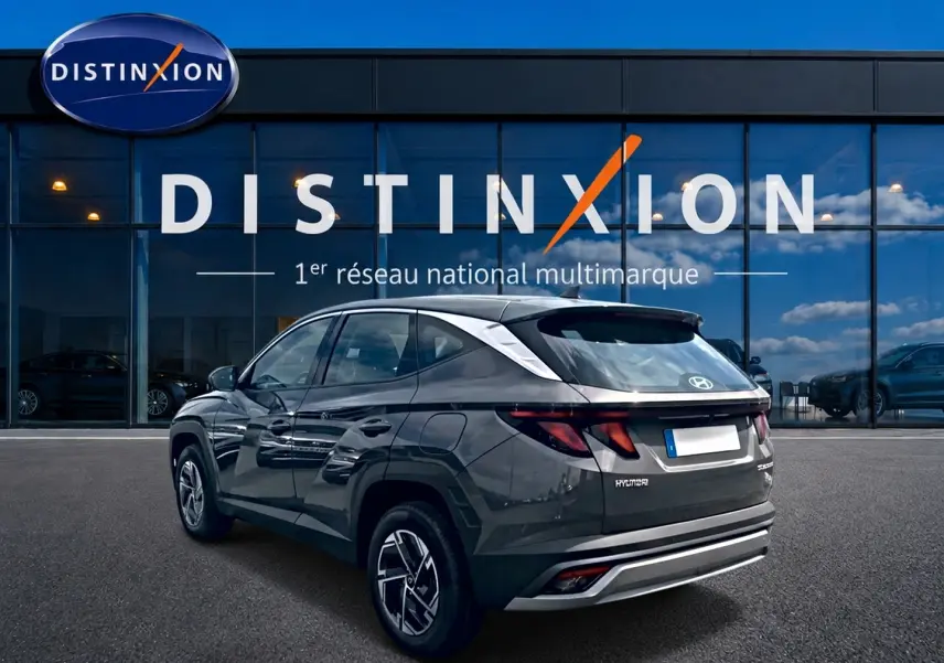 Vue 3/4 arrière droite d'un Hyundai Tucson gris ecotronique avec jantes alliage et feux arrière LED, devant une vitrine Distinxion.
