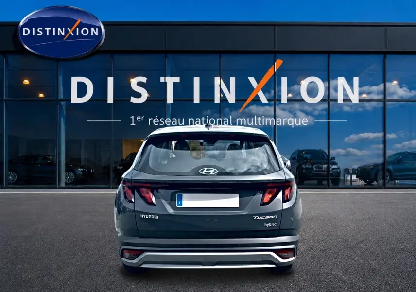 Vue arrière d’un Hyundai Tucson hybride gris écotronique garé devant une vitrine Distinxion avec logo visible.
