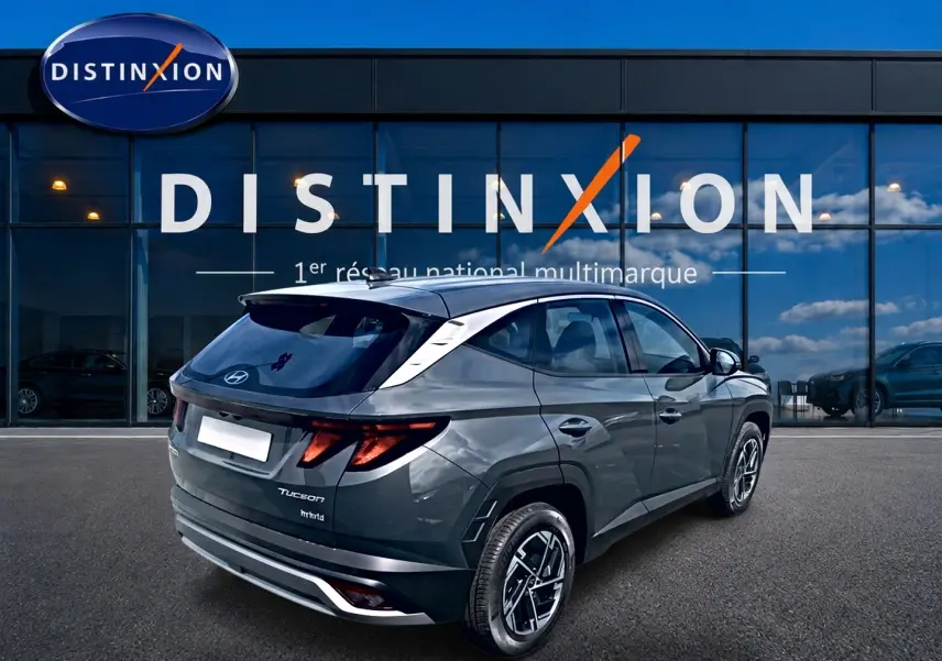 Vue 3/4 arrière droite d'un Hyundai Tucson 2026 gris ecotronique avec jantes alliage et vitres teintées devant un showroom Distinxion.