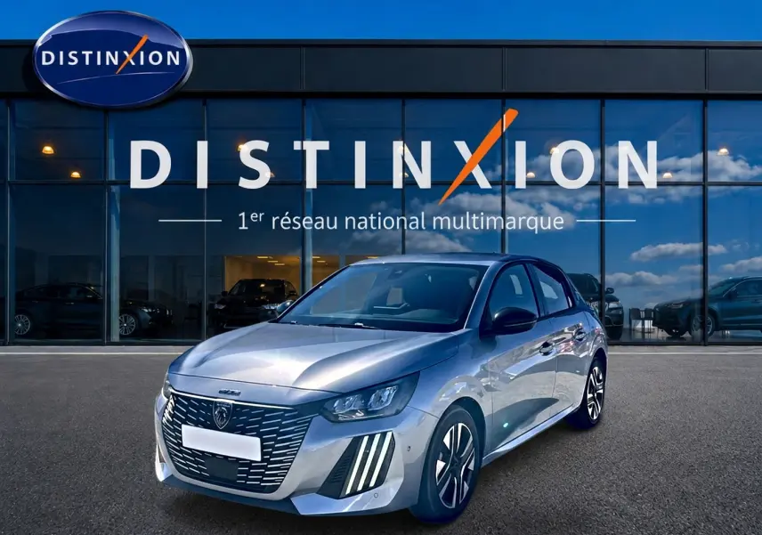 Peugeot 208 1.2 100 Allure gris Artense vue 3/4 avant avec calandre distinctive et jantes alu devant un showroom Distinxion.