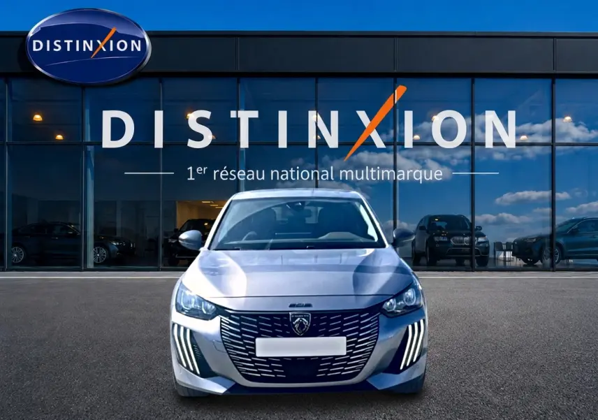 Vue frontale d'une Peugeot 208 1.2 100 Allure gris Artense devant une vitrine avec logo Distinxion.