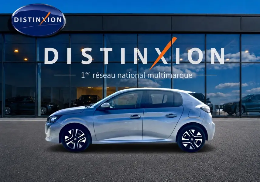 Profil côté gauche de la Peugeot 208 1.2 100 Allure gris Artense, avec jantes alliage et vitres teintées, devant une vitrine Distinxion.