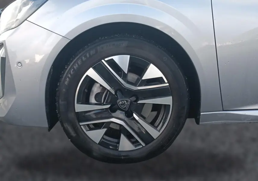 Gros plan sur la roue avant gauche de la Peugeot 208 gris artense avec jante alu bicolore et partie avant du véhicule visible.