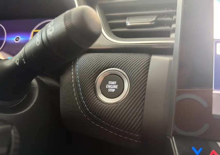 Gros plan sur le bouton Start Engine Stop entouré de tissu noir à surpiqûres bleues dans le tableau de bord du Renault Captur E-Tech.