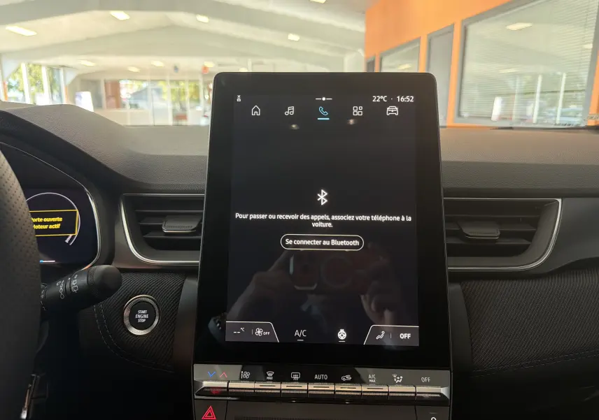Vue intérieure centrée sur l'écran tactile vertical du tableau de bord du Renault Captur E-Tech gris Rafale, avec commandes climatisation visibles.