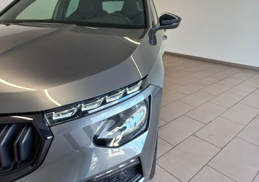 Gros plan sur l’avant droit du Skoda Kamiq Monte Carlo 2024 en gris graphite, mettant en valeur ses phares LED et calandre distinctive.