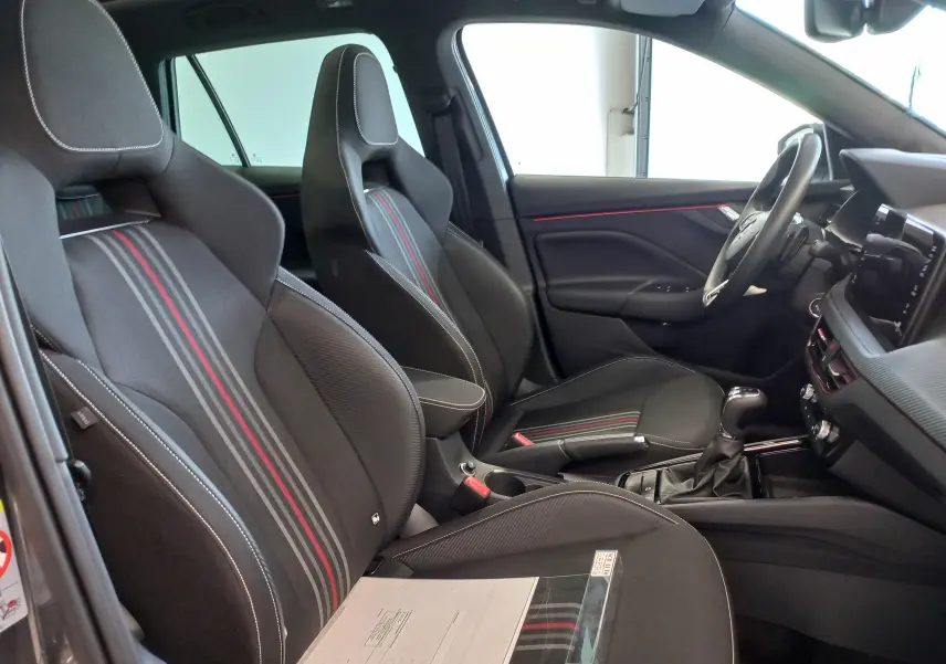 Vue intérieure côté conducteur du Skoda Kamiq Monte Carlo 2024, sièges noirs avec bandes grises et rouges, volant et console visibles.