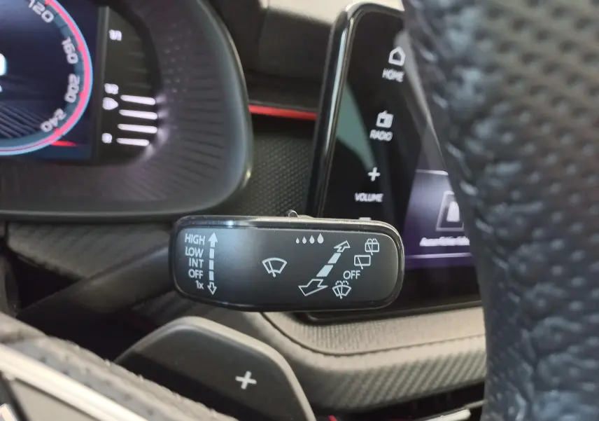 Gros plan sur la commande d’essuie-glace du Skoda Kamiq 2024 gris graphite, avec tableau de bord et écran tactile en arrière-plan.