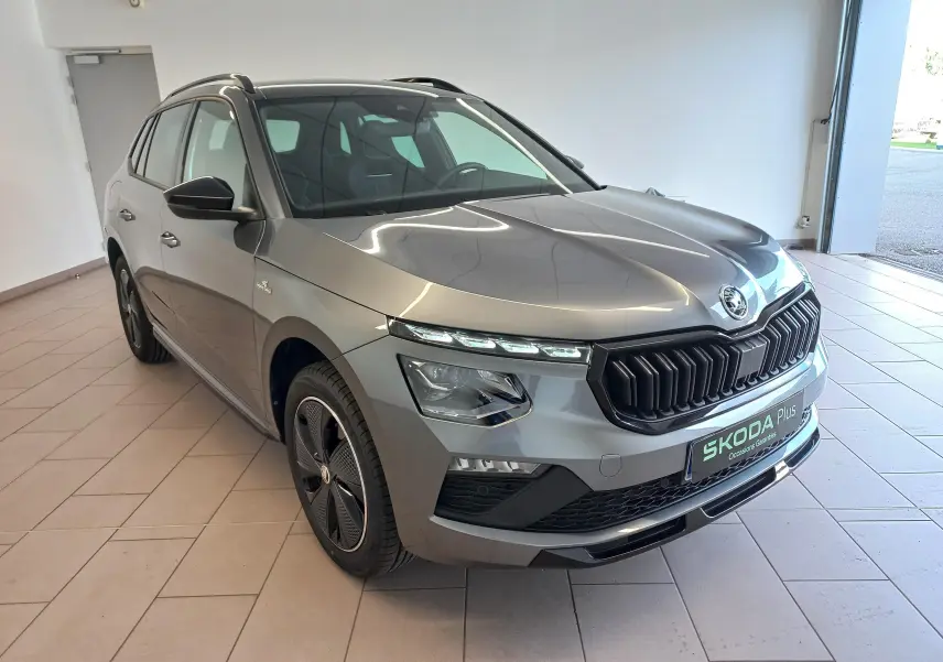 Vue 3/4 avant droite d'un Skoda Kamiq 2024 gris graphite version Monte Carlo avec calandre noire et jantes spécifiques.