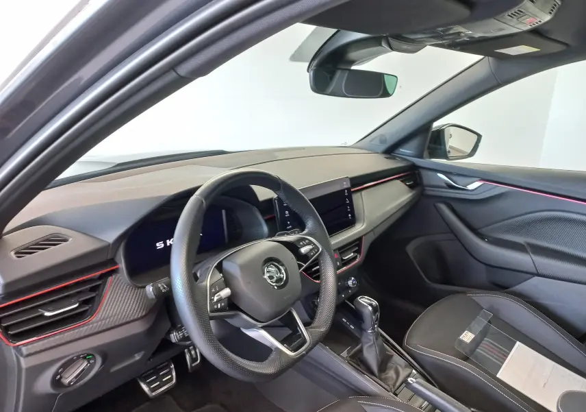 Vue intérieure côté conducteur du Skoda Kamiq 2024 gris graphite, avec éclairage d'ambiance rouge et tableau de bord moderne.