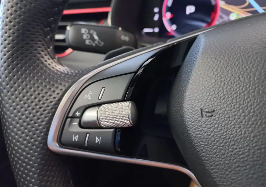 Gros plan sur la partie gauche du volant perforé du Skoda Kamiq 2024 gris graphite, avec commandes audio et molette métallique.
