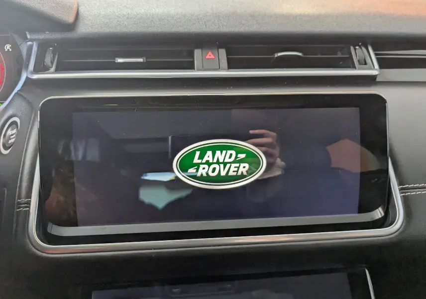 Écran tactile central allumé avec logo Land Rover dans l'habitacle noir du Range Rover Velar 2020.