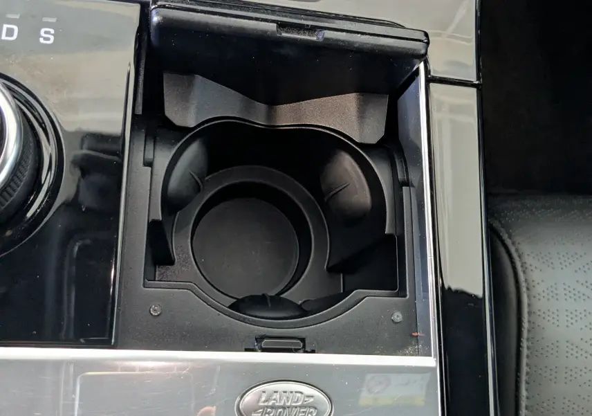 Gros plan sur la console centrale noire du Range Rover Velar 2020 avec porte-gobelets et logo Land Rover argenté.