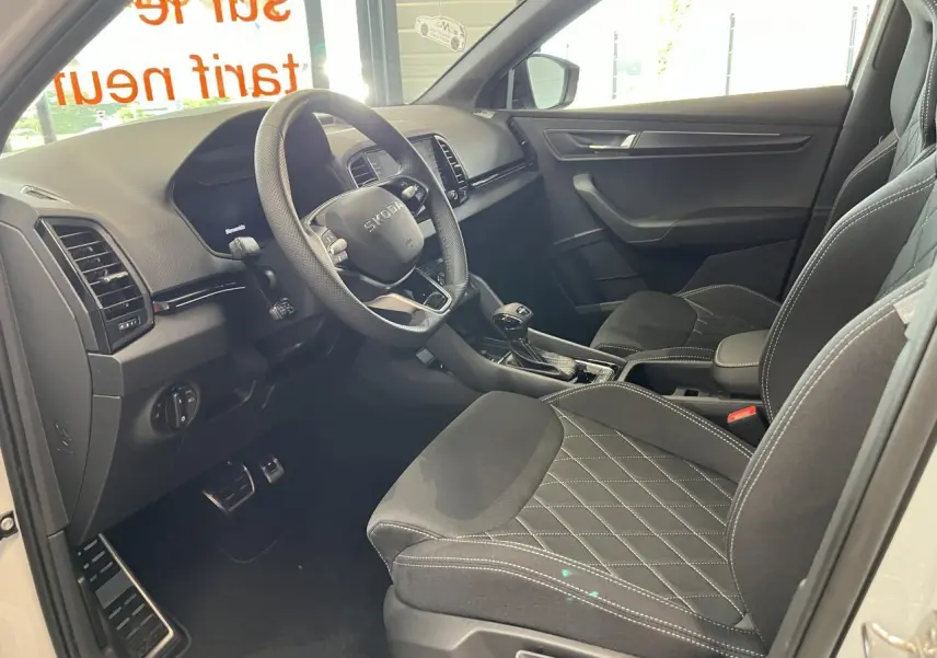 Intérieur avant droit du Skoda Karoq blanc 2025, sellerie noire Sportline avec surpiqûres blanches et volant cuir multifonctions.