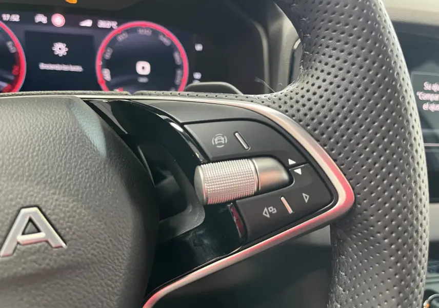 Gros plan sur le volant perforé noir avec commandes multifonctions et tableau de bord digital rouge du Skoda Karoq Sportline 2025.