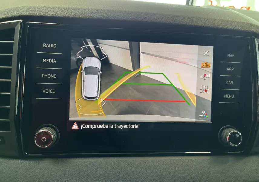Écran tactile intérieur montrant la caméra de recul et l’aide au stationnement du Skoda Karoq blanc, vue de face.