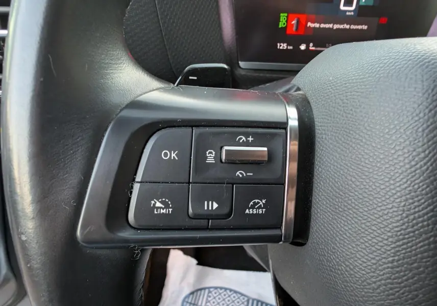 Gros plan sur les commandes au volant à gauche de la Citroën C4 2022, avec affichage numérique en arrière-plan.